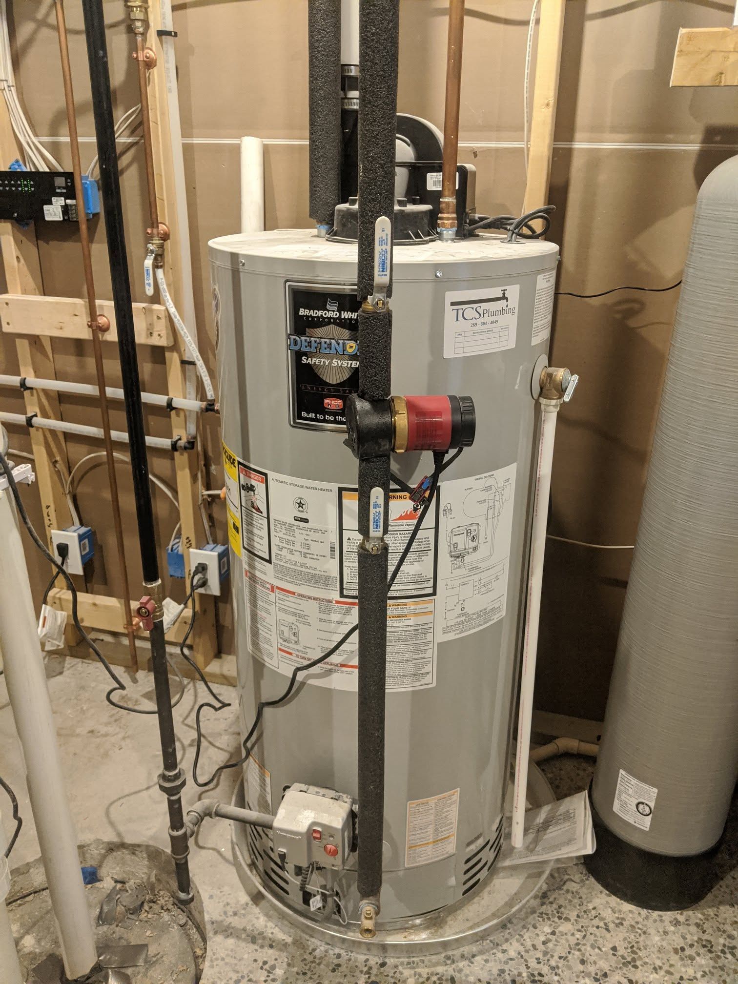 Water heater in a utility basement with pipes, valves, and surrounding plumbing equipment.
