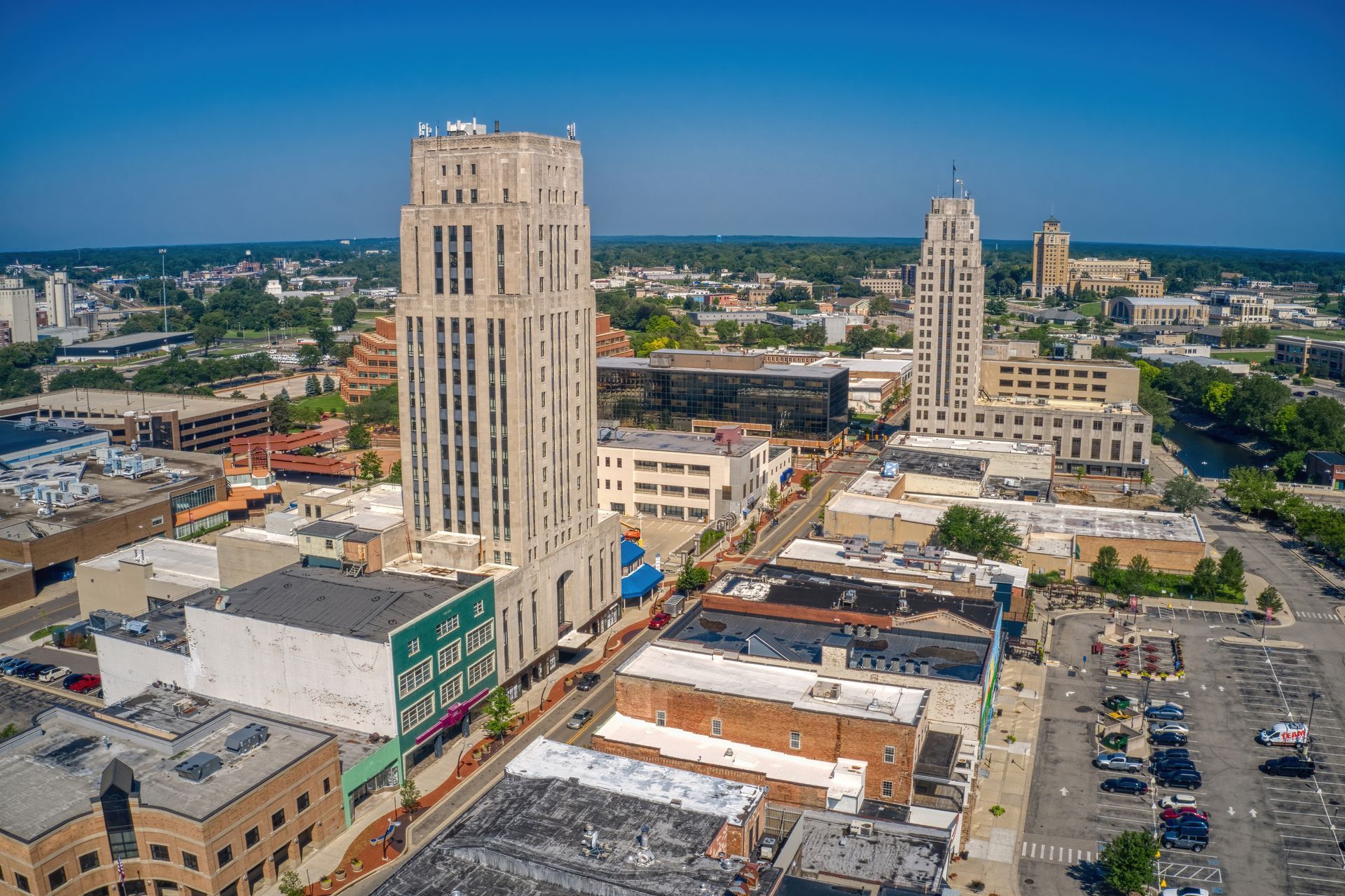 Aerial view of a downtown Battle Creek, MI with tall buildings, streets, and parking lots under a clear blue sky