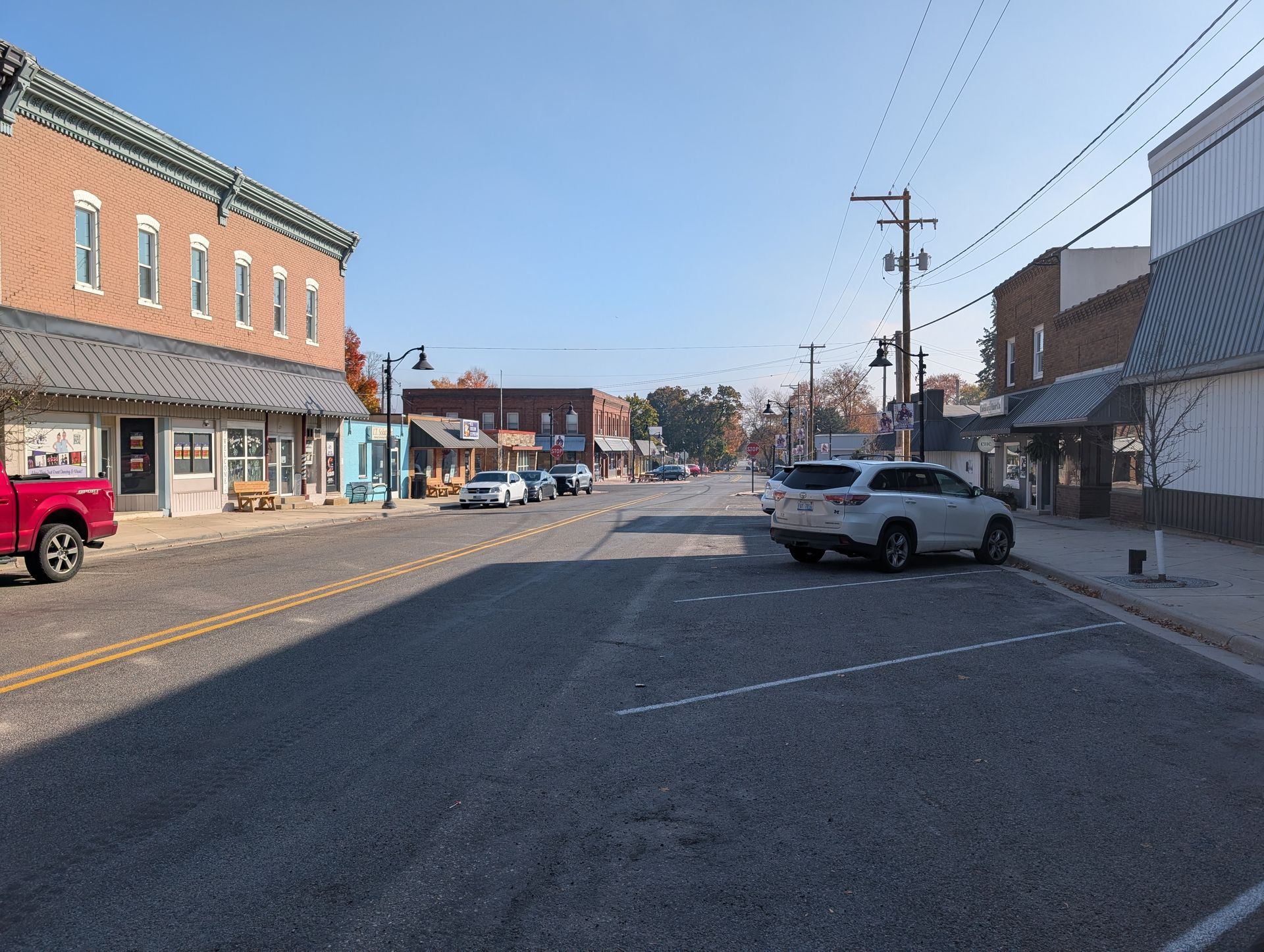 Caledonia, MI main street with storefronts, parked cars, and a wide empty road under a clear sky
