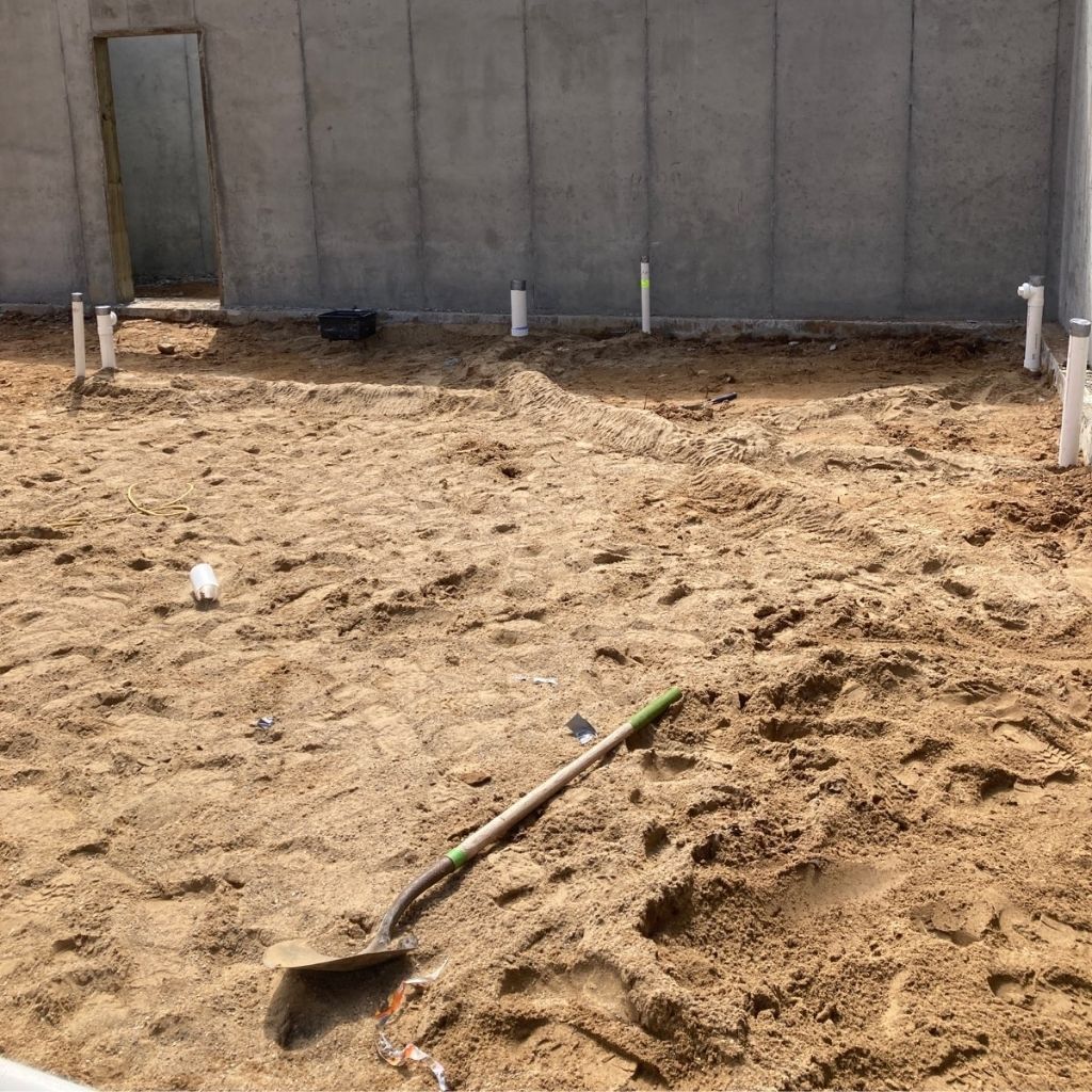 Sandy construction site with a shovel in the foreground and concrete walls in the background