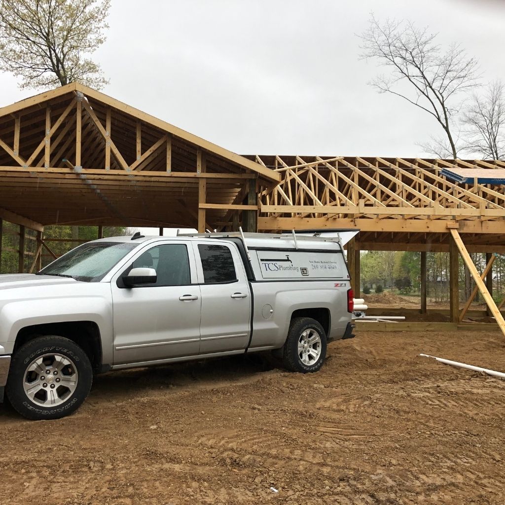Silver pickup truck parked beside a partly built wooden house frame under a cloudy sky