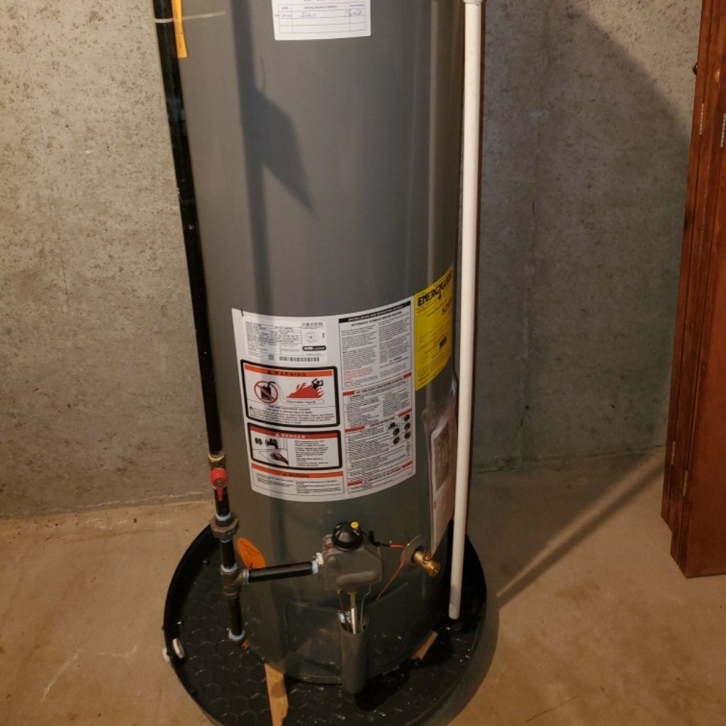 Gray water heater tank with warning labels and plumbing pipes in a basement or utility area