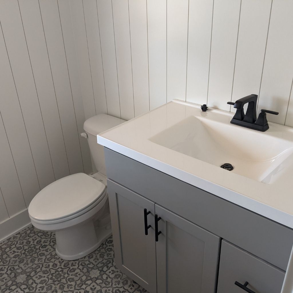Small bathroom with a white toilet, gray vanity, and sink with black faucet against striped walls.