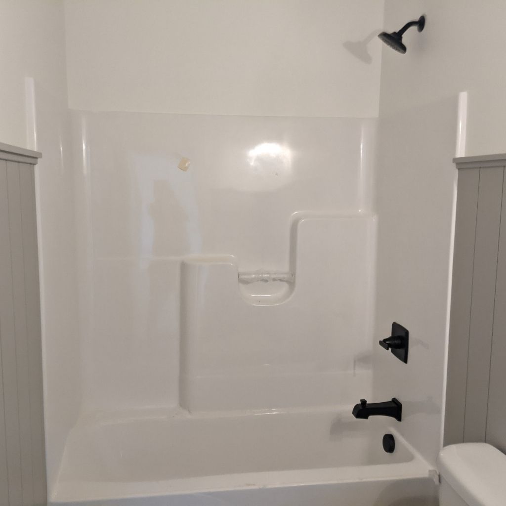 White bathtub shower alcove with grab bar, black fixtures, and a built-in soap shelf