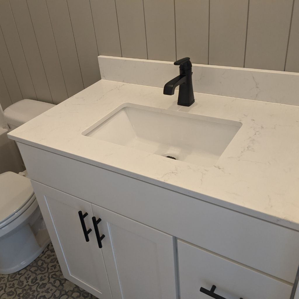 White bathroom vanity with sink and black faucet, shown beside a toilet.