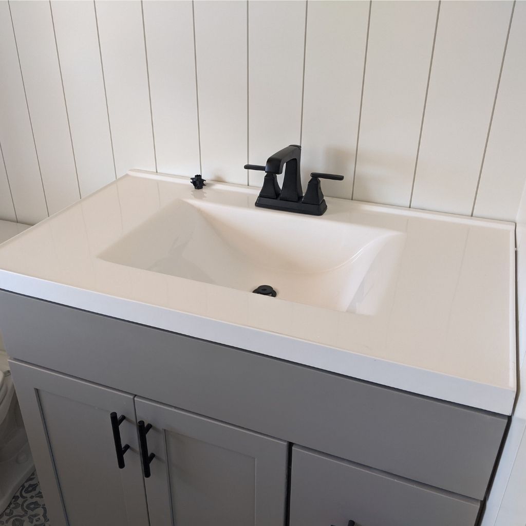 White bathroom vanity with rectangular sink and black faucet against white paneled wall.