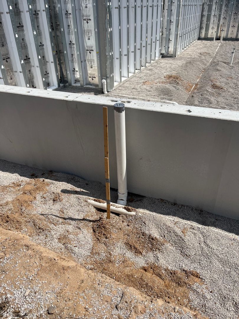 Damaged metal siding with a leaking pipe over muddy ground near a concrete wall