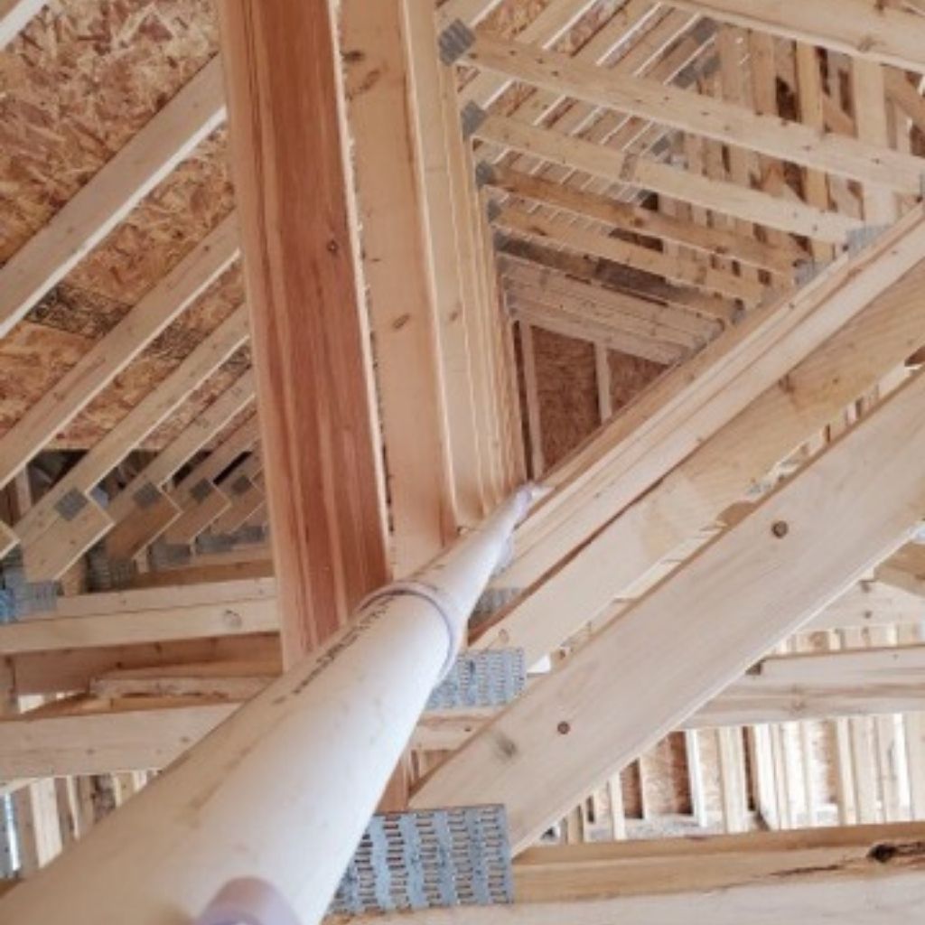 Interior of a house under construction, showing wooden roof trusses and framing.