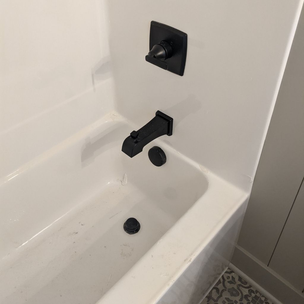 Bathtub with matte black faucet and shower controls against white tile wall