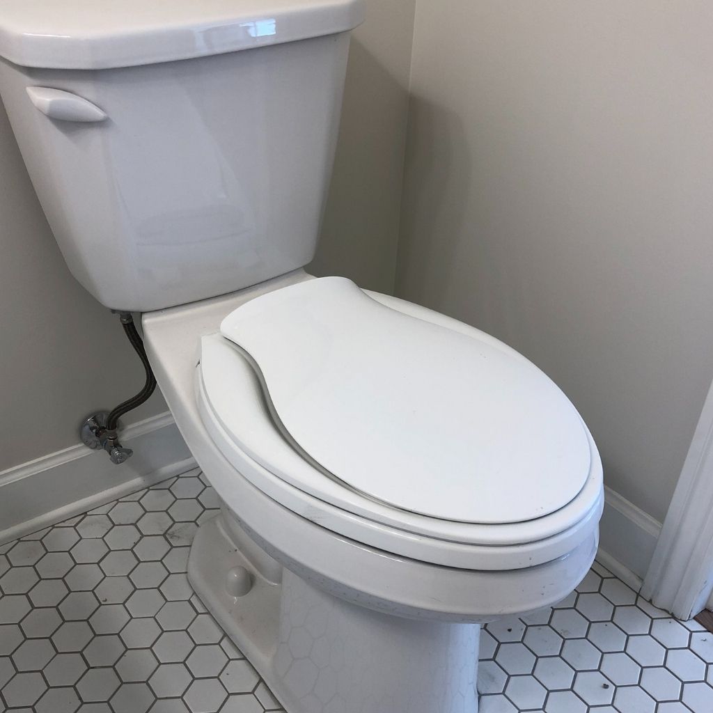 White toilet in a small bathroom with hexagon tile floor and gray walls.