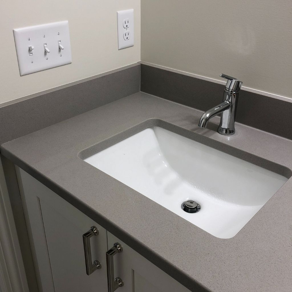 Small bathroom sink with gray countertop, chrome faucet, and wall-mounted soap/dispenser outlets