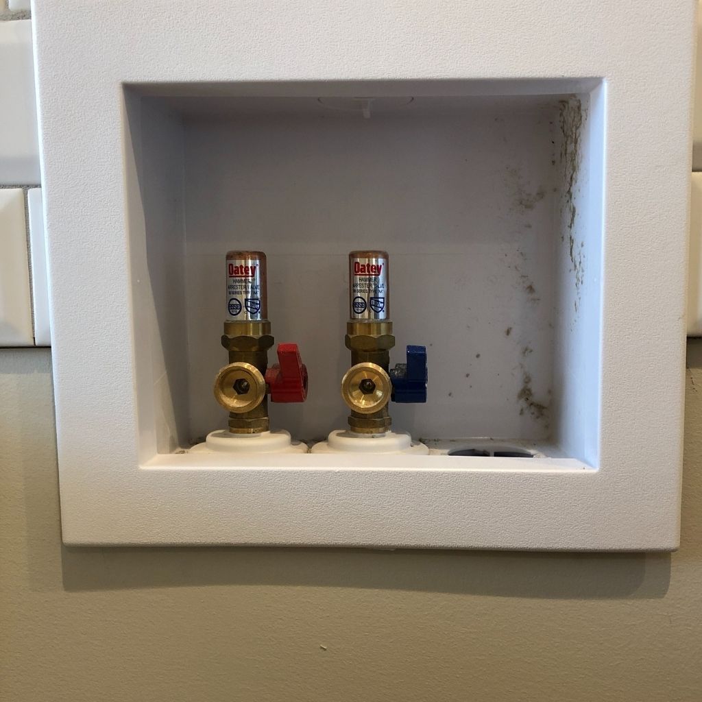 Wall recessed plumbing box with two brass water valves, red and blue shutoff handles, and capped pipes