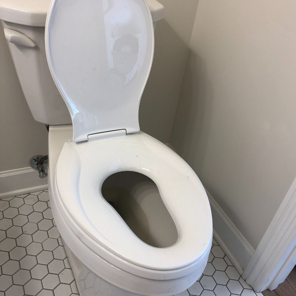 White toilet with lid and seat up in a small bathroom with hexagon tile floor