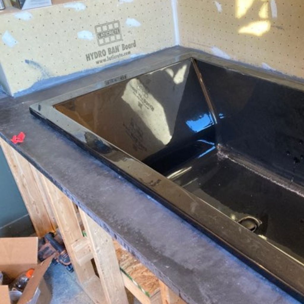 Black kitchen sink set into a countertop with unfinished drywall and construction materials nearby