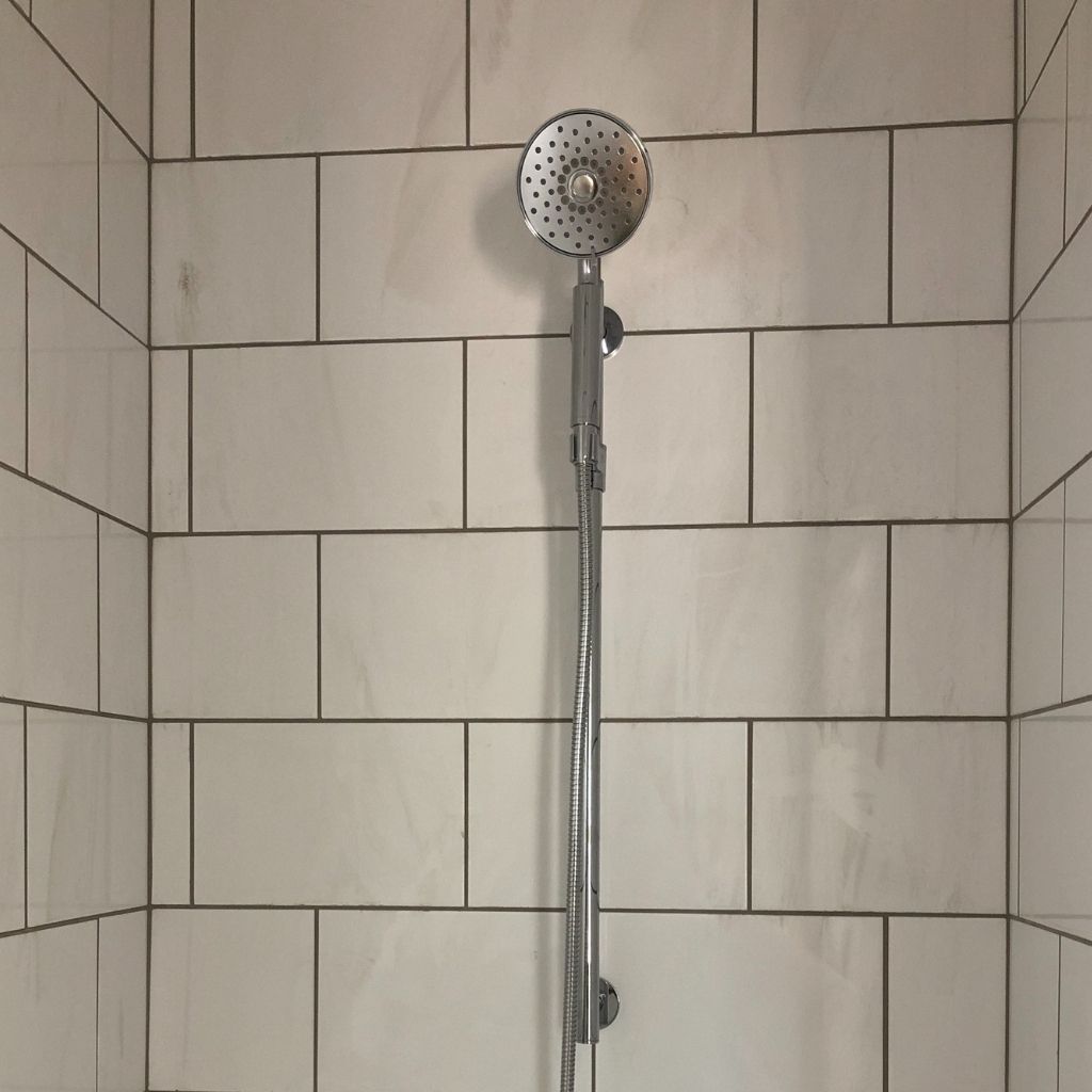 Handheld showerhead mounted on a chrome bar in a tiled shower stall