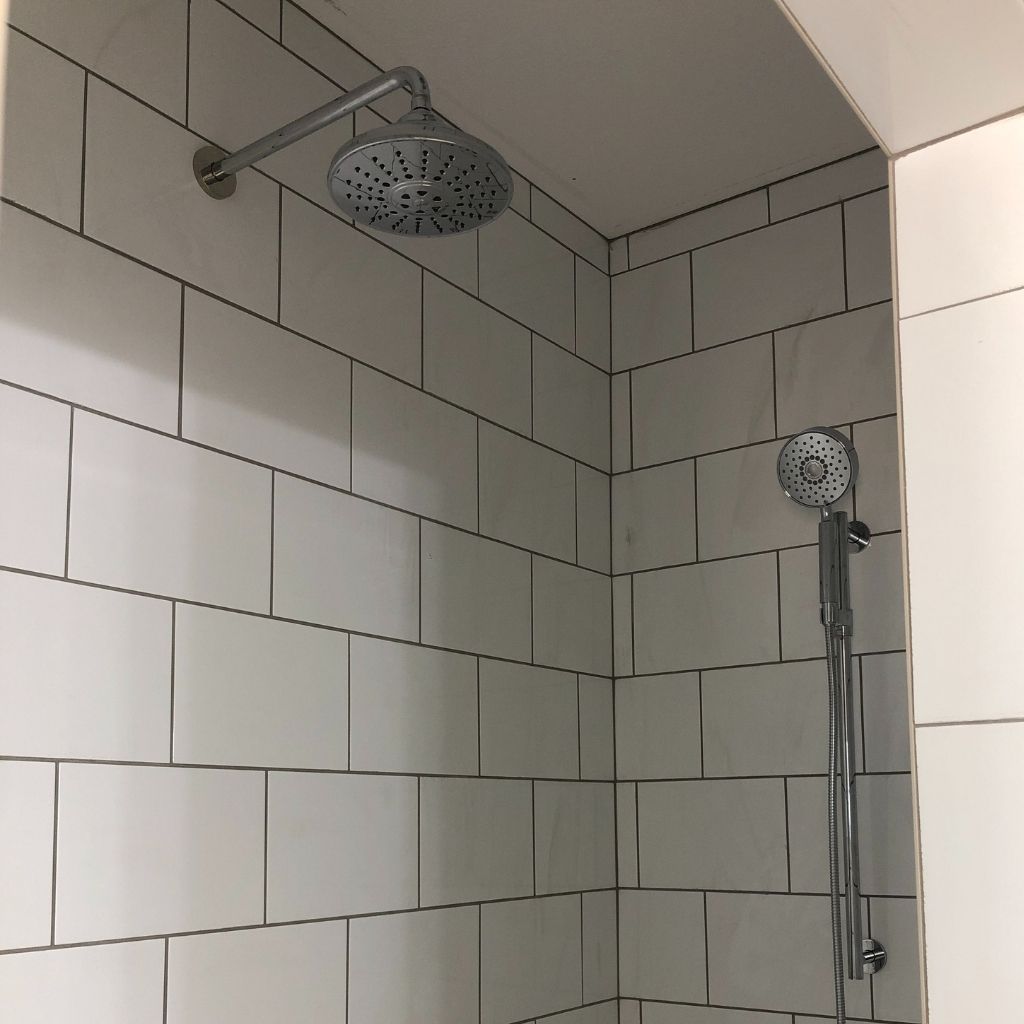 Tiled shower with two chrome showerheads, white walls, and no people