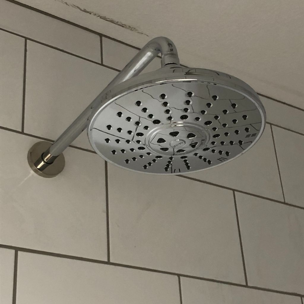 Chrome showerhead mounted on a tiled bathroom wall, angled downward.