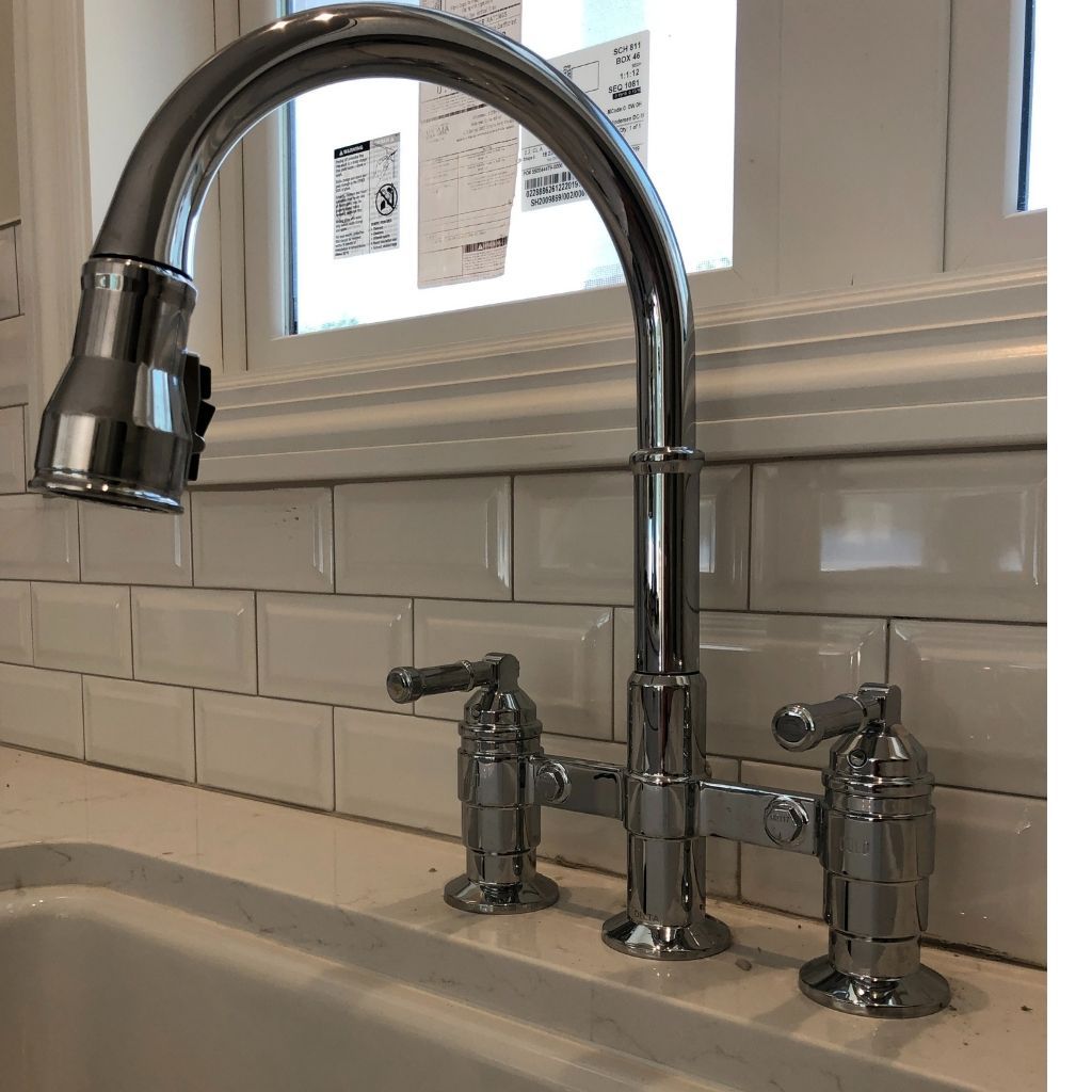 Chrome kitchen faucet over sink with white subway tile backsplash and two soap dispensers
