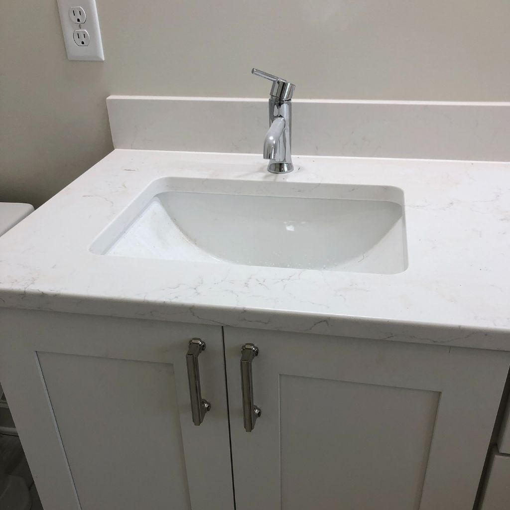 White bathroom vanity with integrated sink and chrome faucet against a light wall.