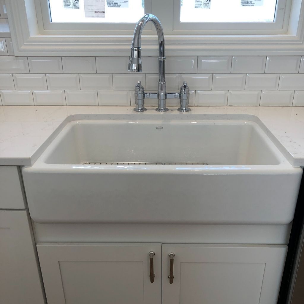 White farmhouse sink with chrome faucet above a cabinet in a bright kitchen.
