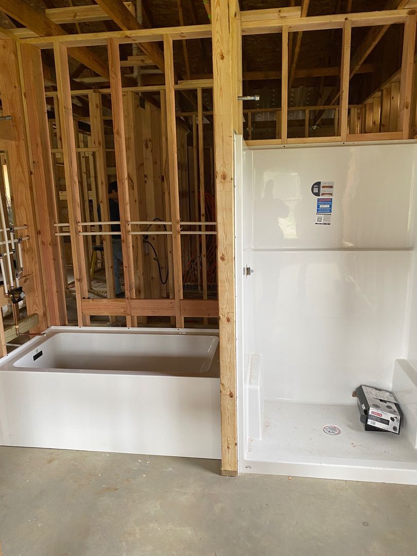 Unfinished bathroom with exposed studs, a white tub, and a white refrigerator beside it.