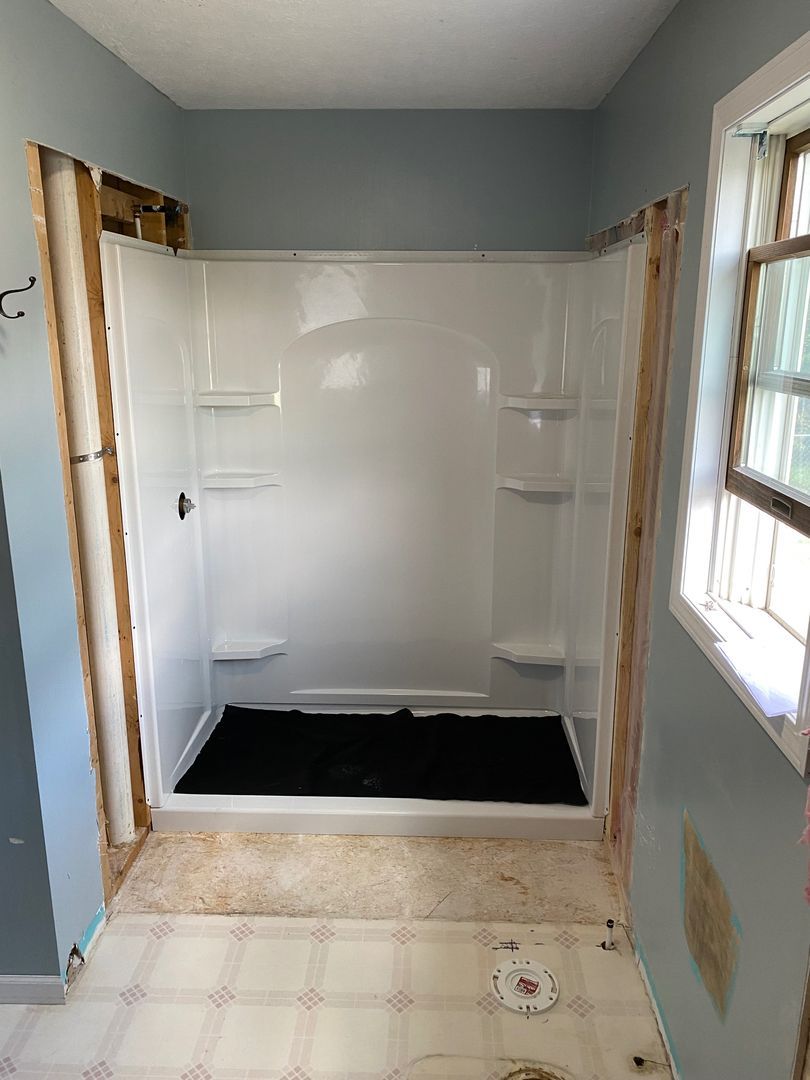 Empty tiled walk-in shower with white walls and a black shower pan in a small bathroom