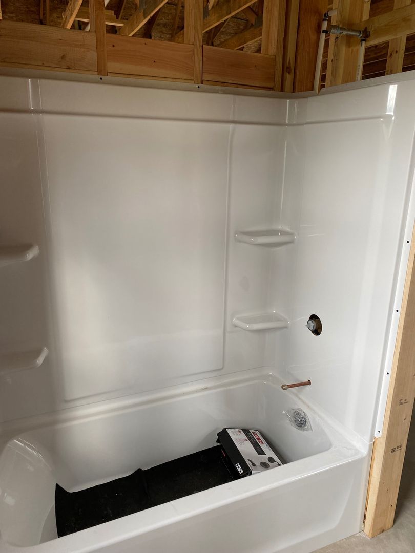 Empty white shower stall with built-in shelves and a black tub mat.