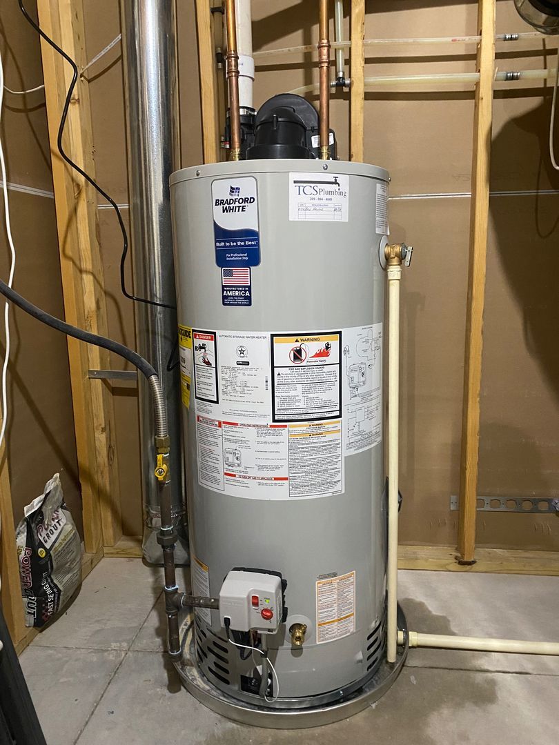 Water heater in a utility closet with exposed pipes and wiring on unfinished walls.