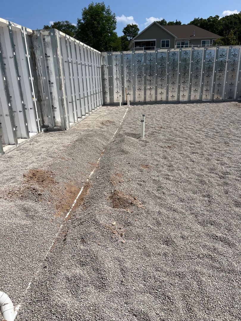 Concrete foundation inside a partially built wooden fence, with houses and trees in the background.