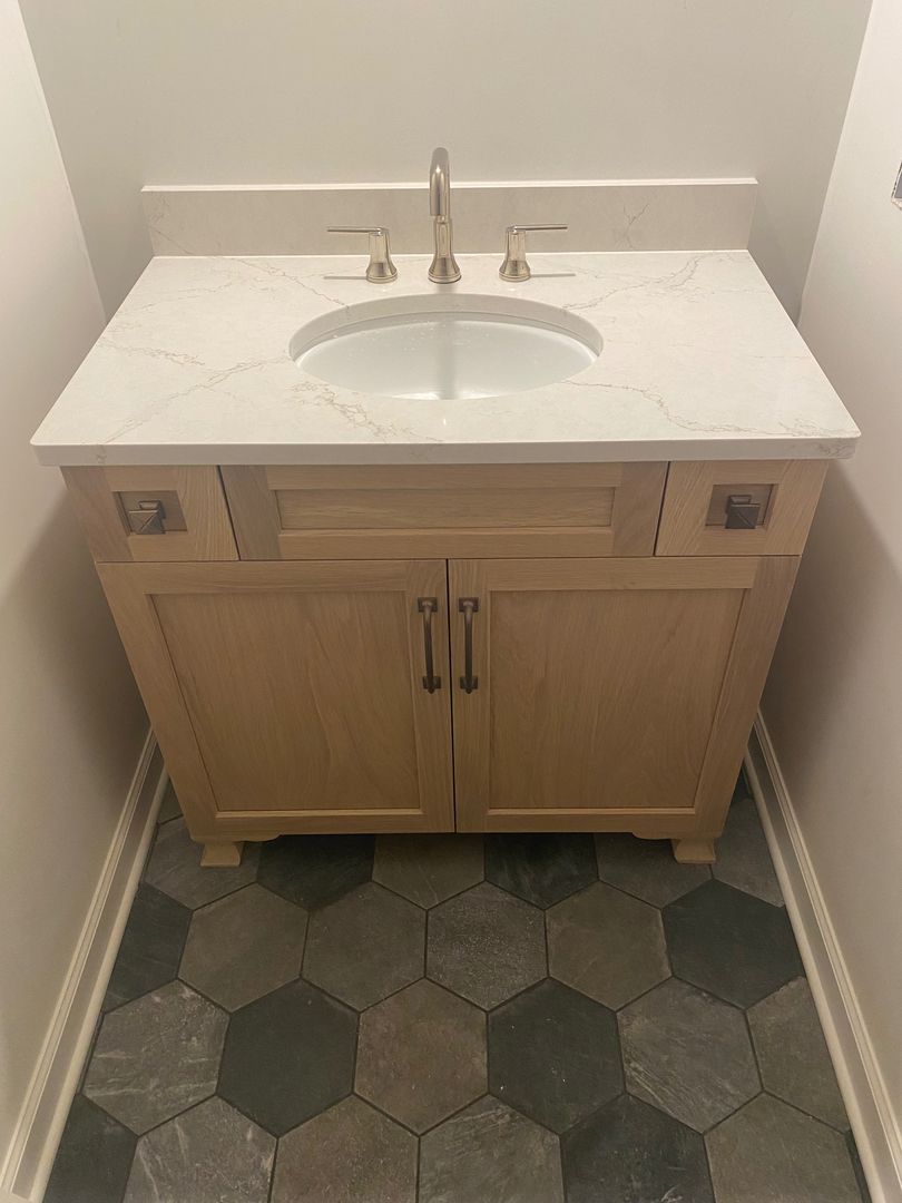 Small bathroom vanity with white sink and wooden cabinet over hexagon tile floor.