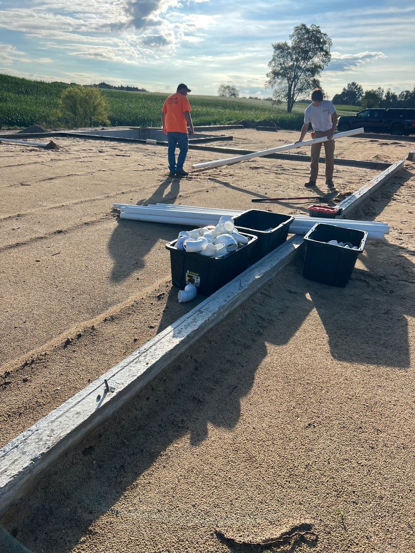 Two workers standing on an airstrip near a small aircraft wing and equipment under a bright sky