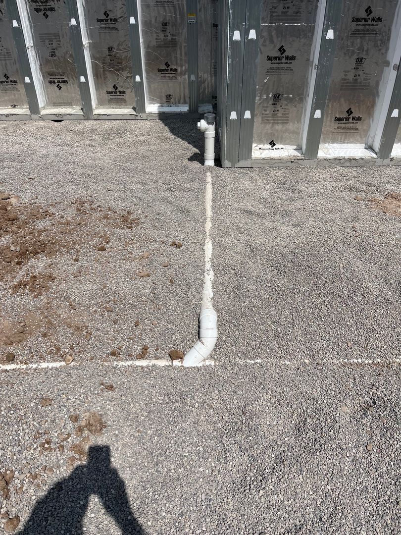 Concrete patio with a white pipe running from the wall to the ground, in front of metal utility doors.