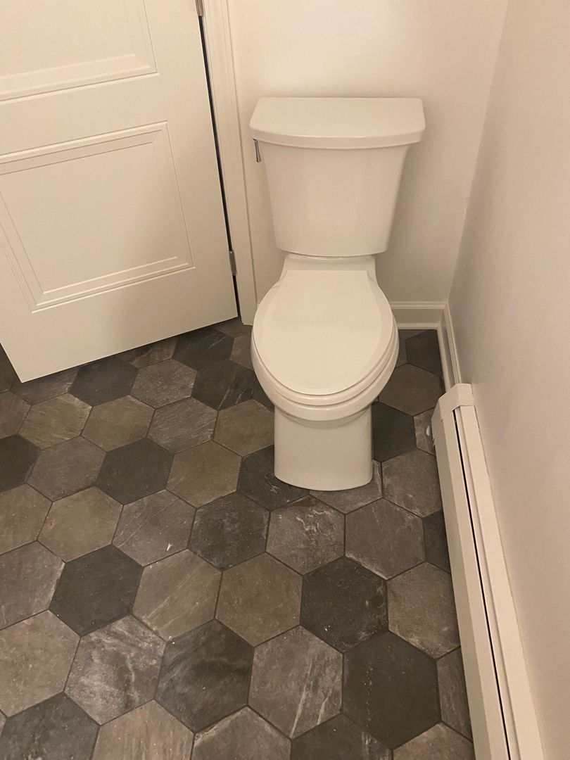 Small bathroom with a white toilet on gray hexagonal tile floor, beside a louvered cabinet.