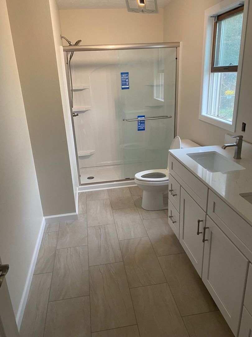 Bathroom with double vanity, large mirror, window, and walk-in shower at the end.