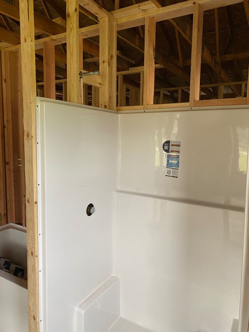 Unfinished bathroom with white shower walls and exposed wooden framing above.