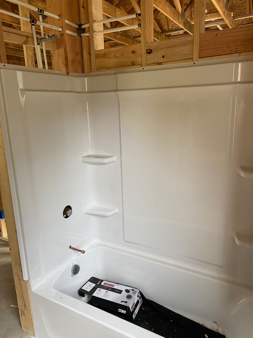 White shower stall with built-in corner shelves in an unfinished bathroom under construction