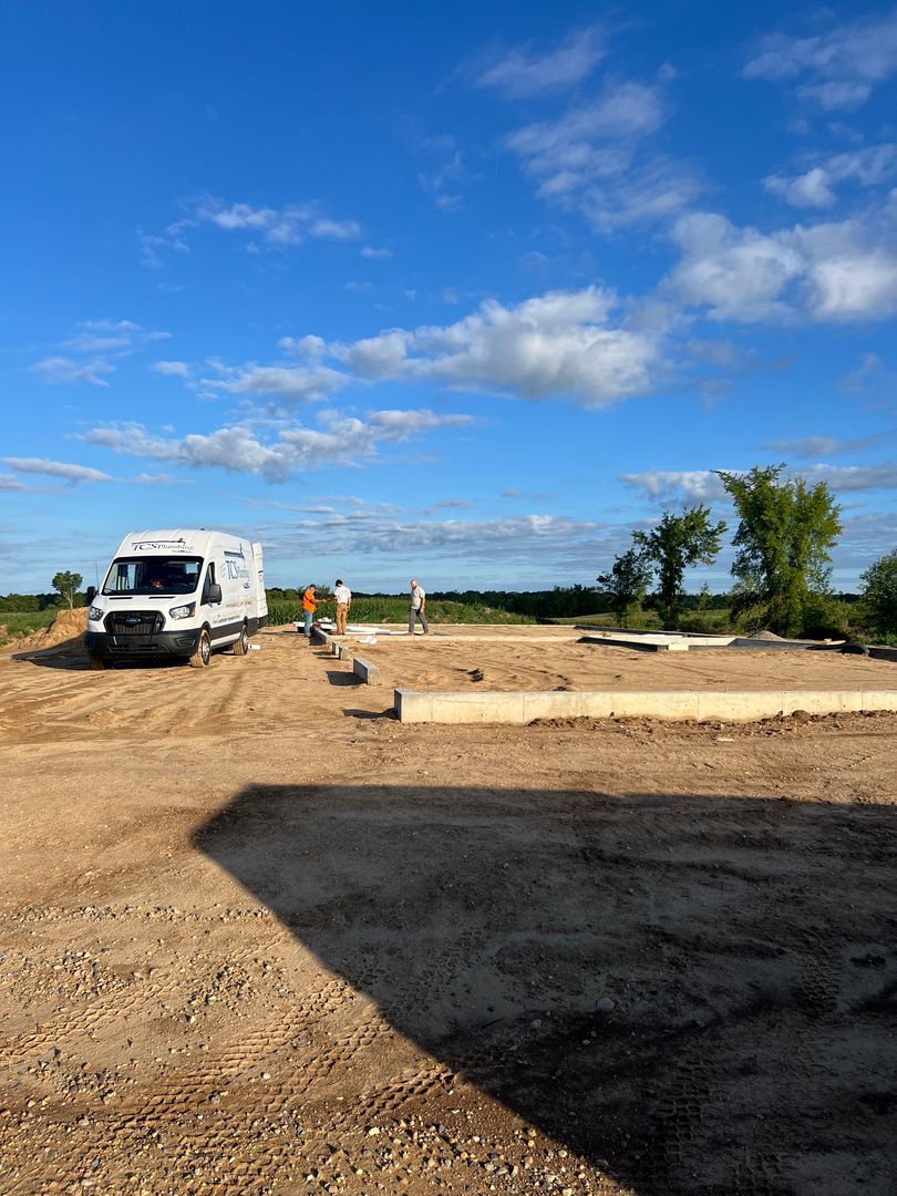 Construction site with a white truck, workers, and foundation forms under a blue sky.