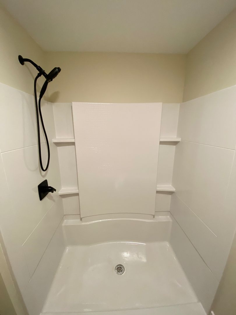 Empty white shower stall with built-in shelves and a handheld showerhead on the left.