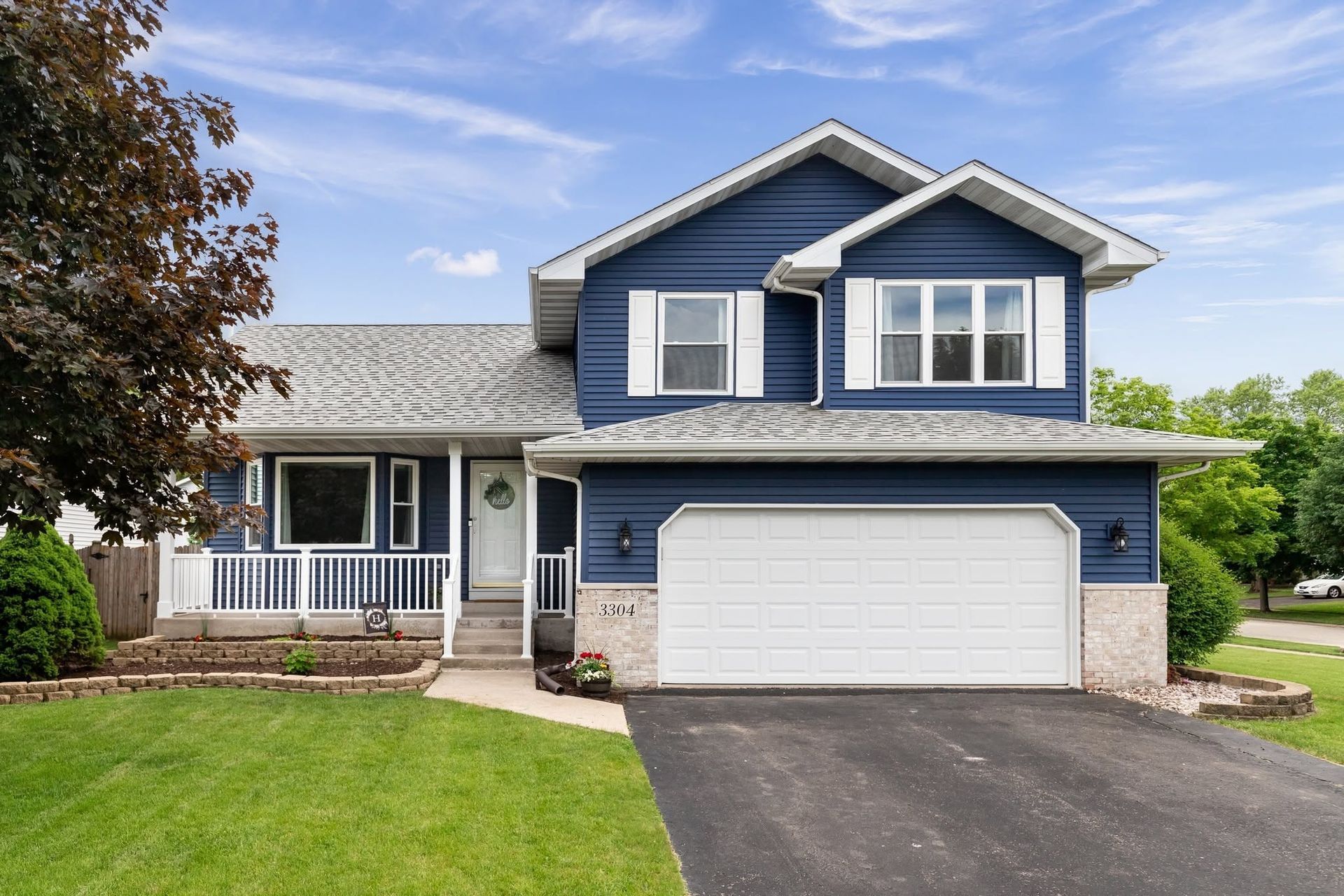 Blue two-story suburban house with white trim, front porch, garage, and green lawn under a partly cloudy sky