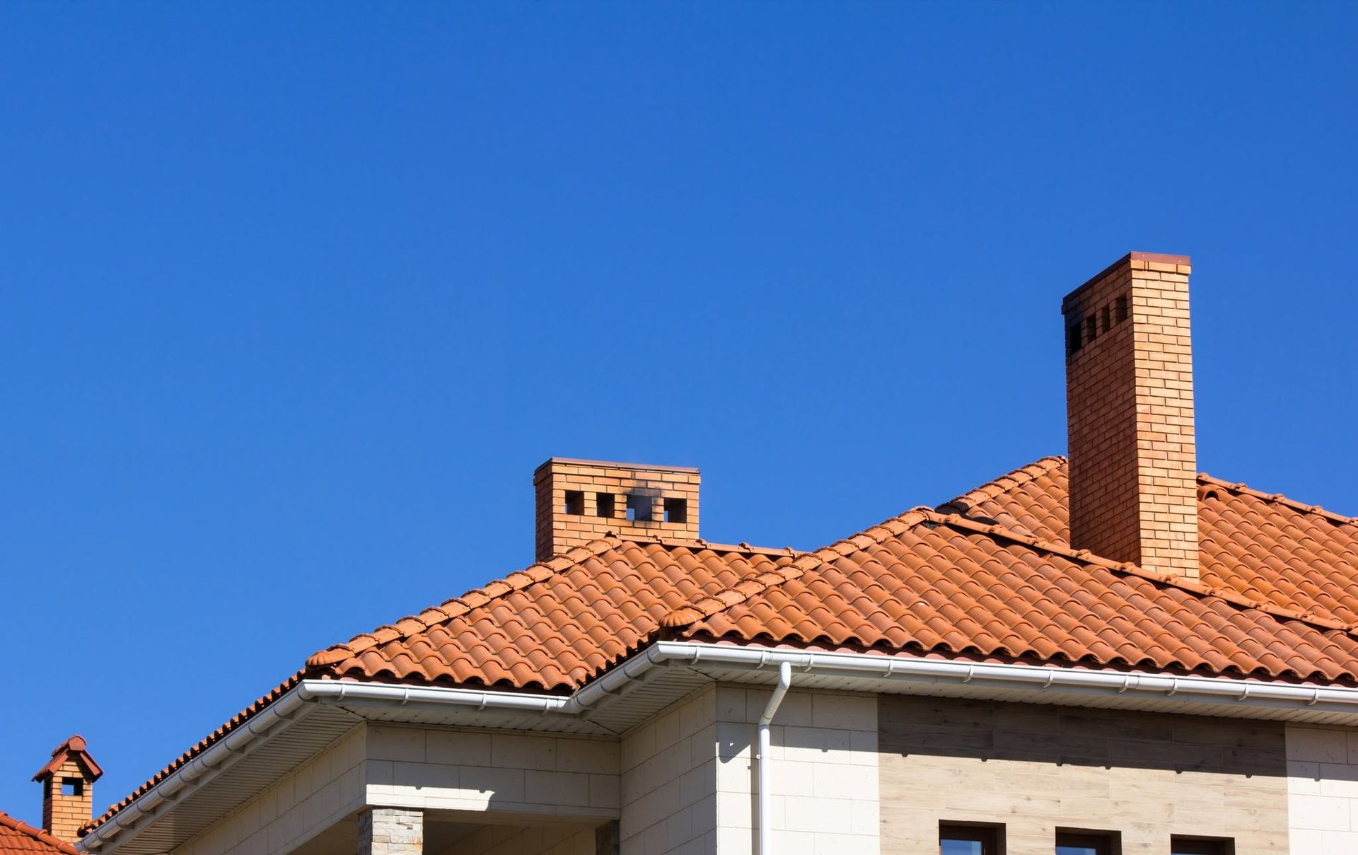 Red-tiled rooftops and brick chimneys against a clear blue sky