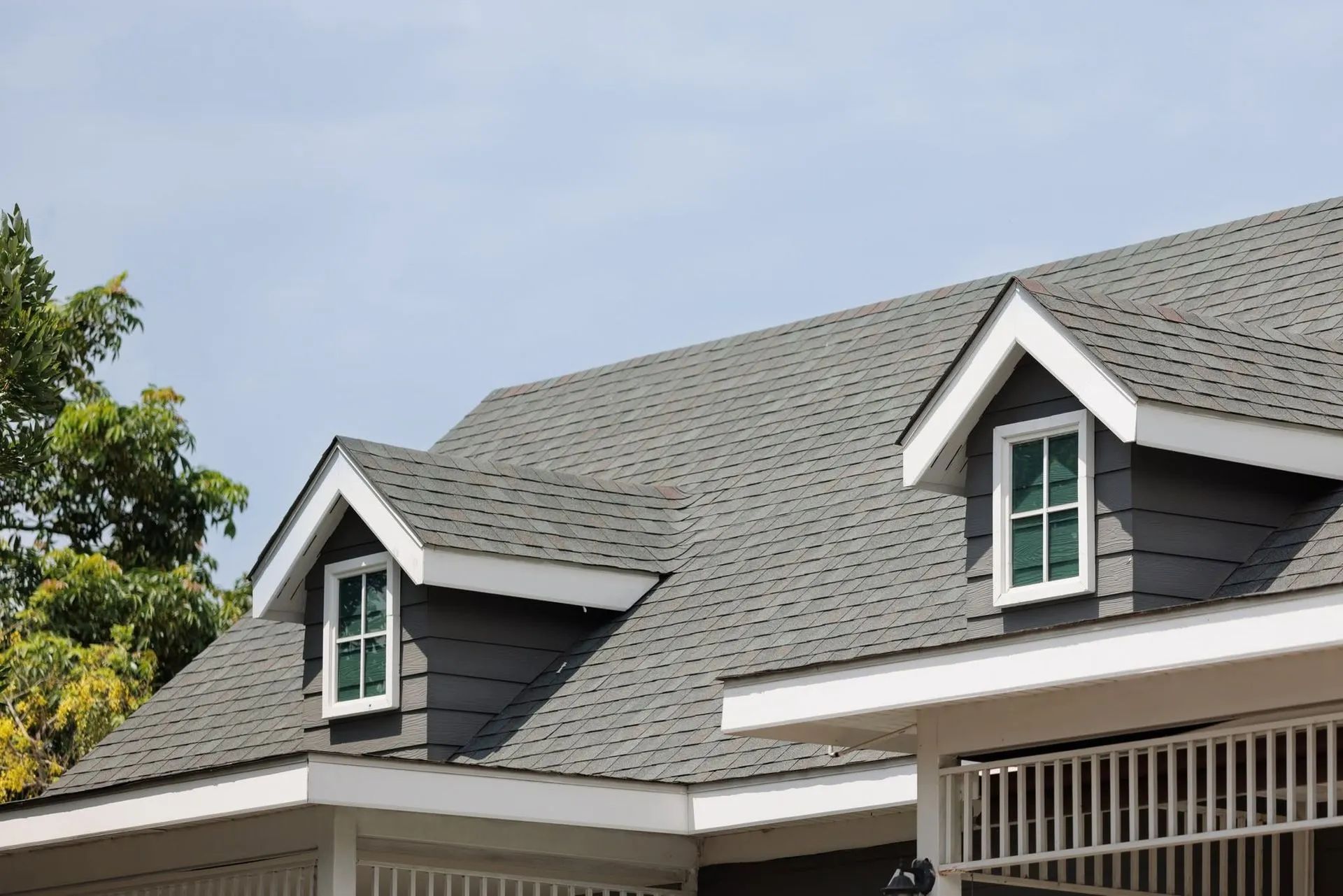 Two dormer windows on a gray shingled house roof against a blue sky