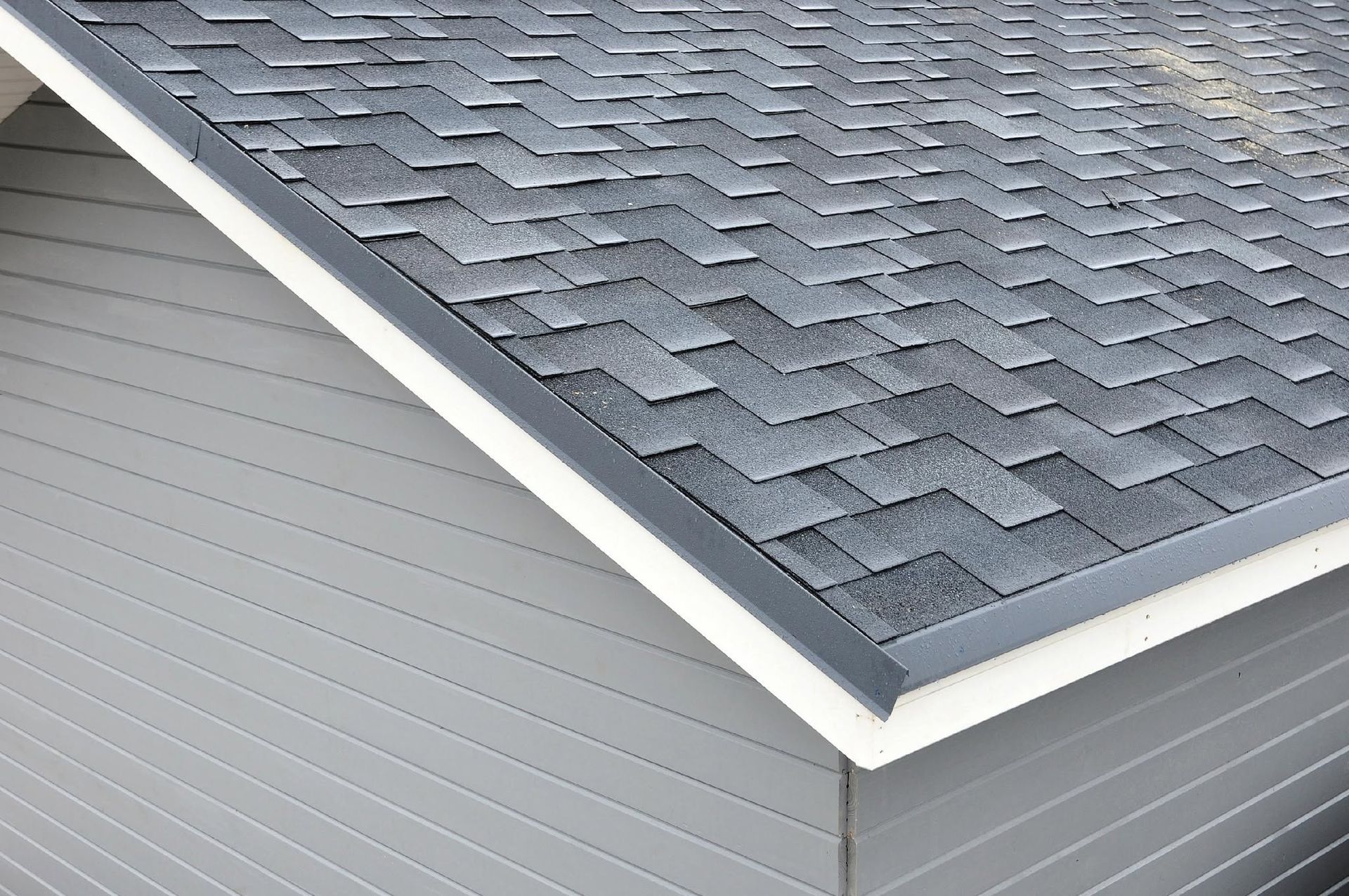 Close-up of a gray shingled roof with white trim and gray siding on a house corner.