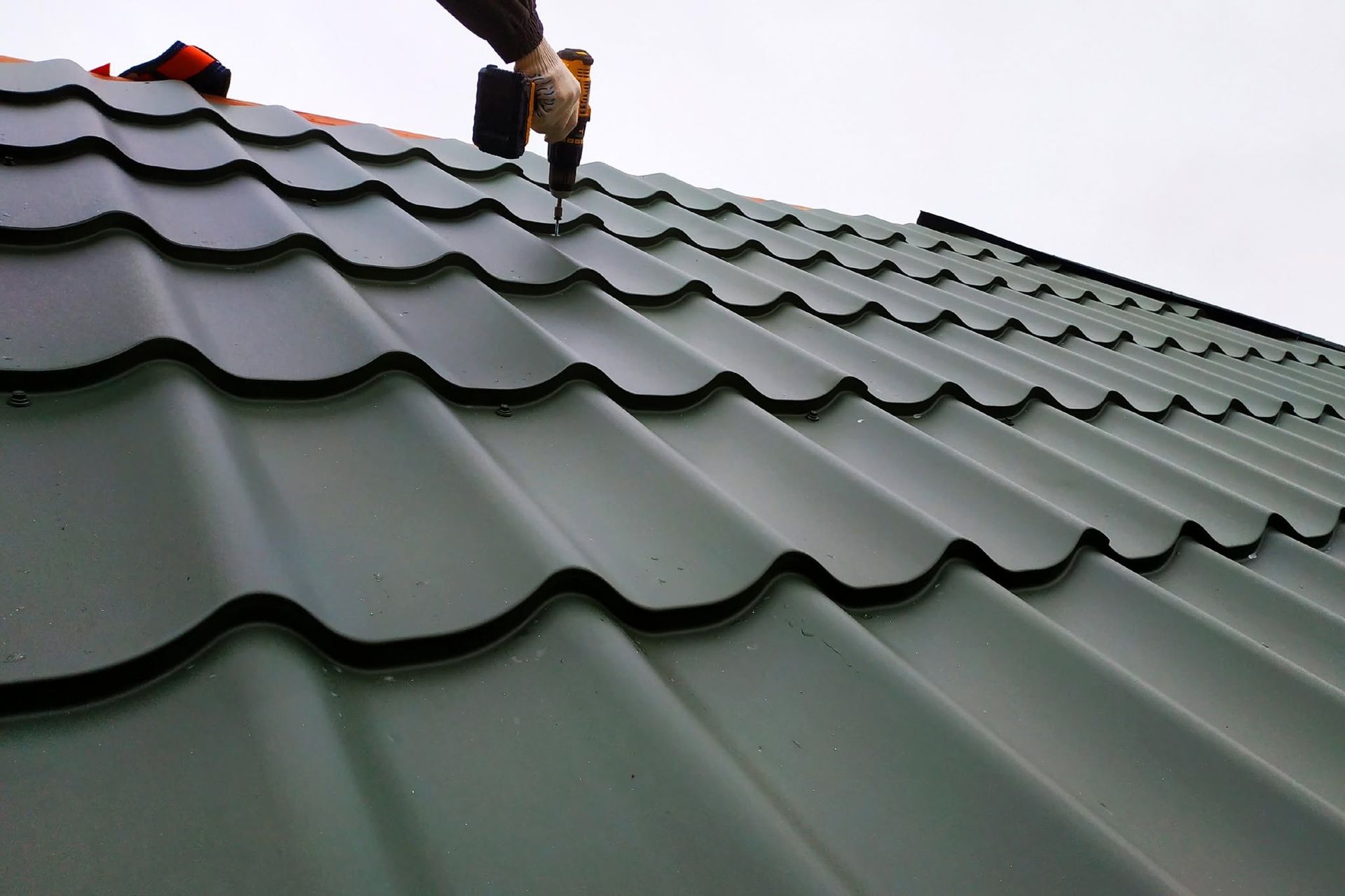 Worker installing green metal roofing on a sloped roof