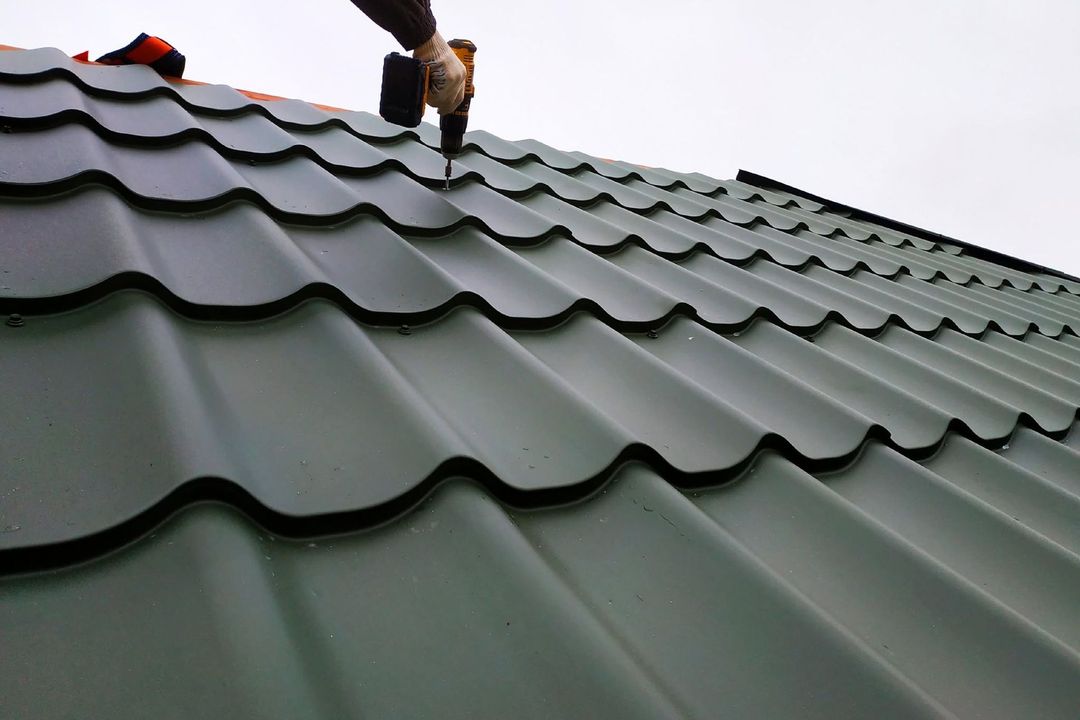 Worker installing green metal roofing on a sloped roof