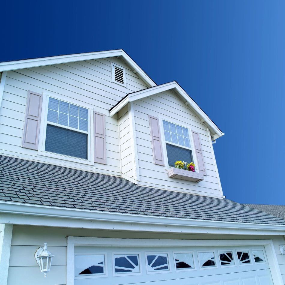 White suburban house exterior with blue sky, shingled roof, garage door, and a flower box under the upstairs window