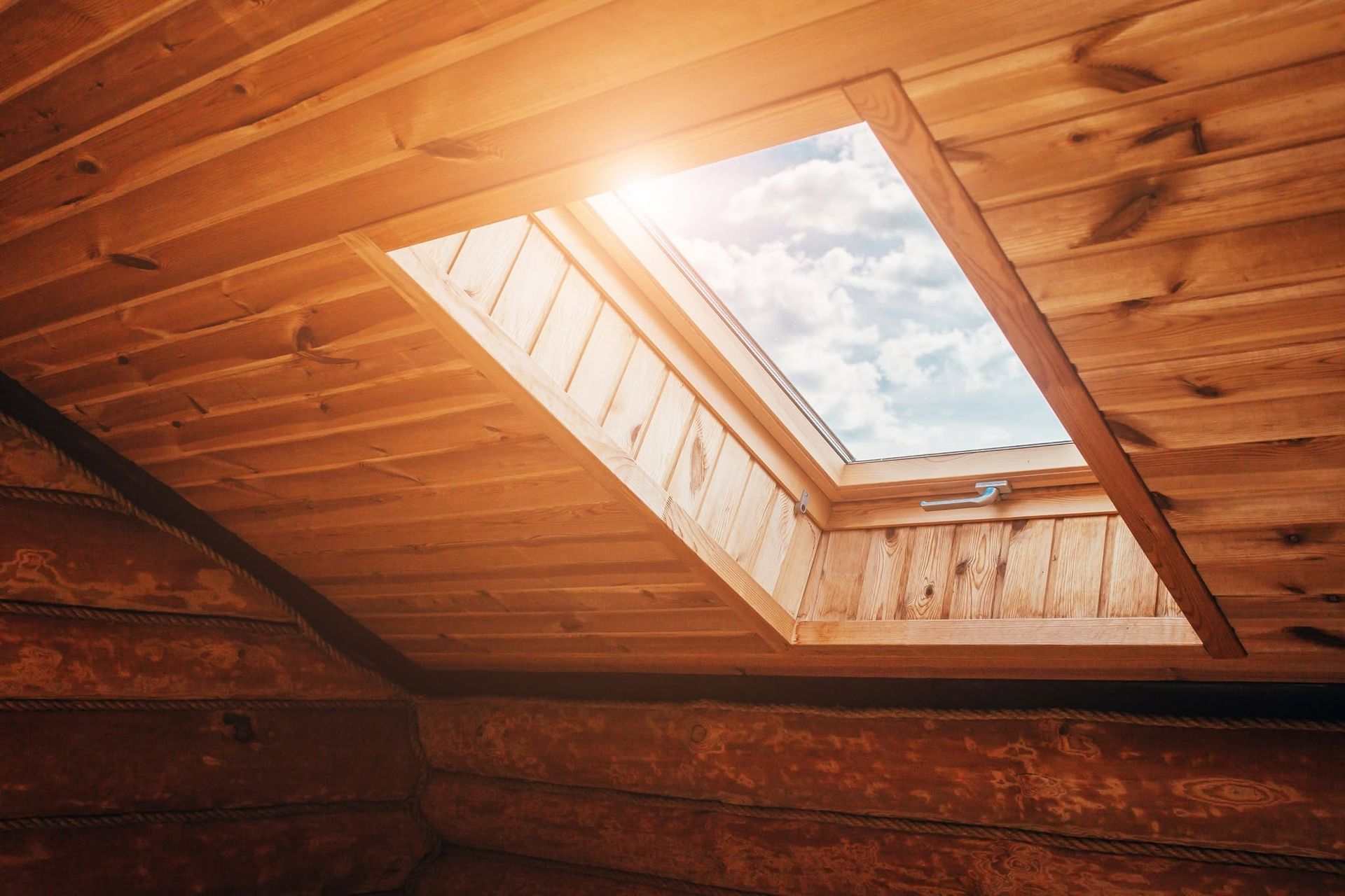Wooden attic interior with an open skylight showing blue sky and clouds