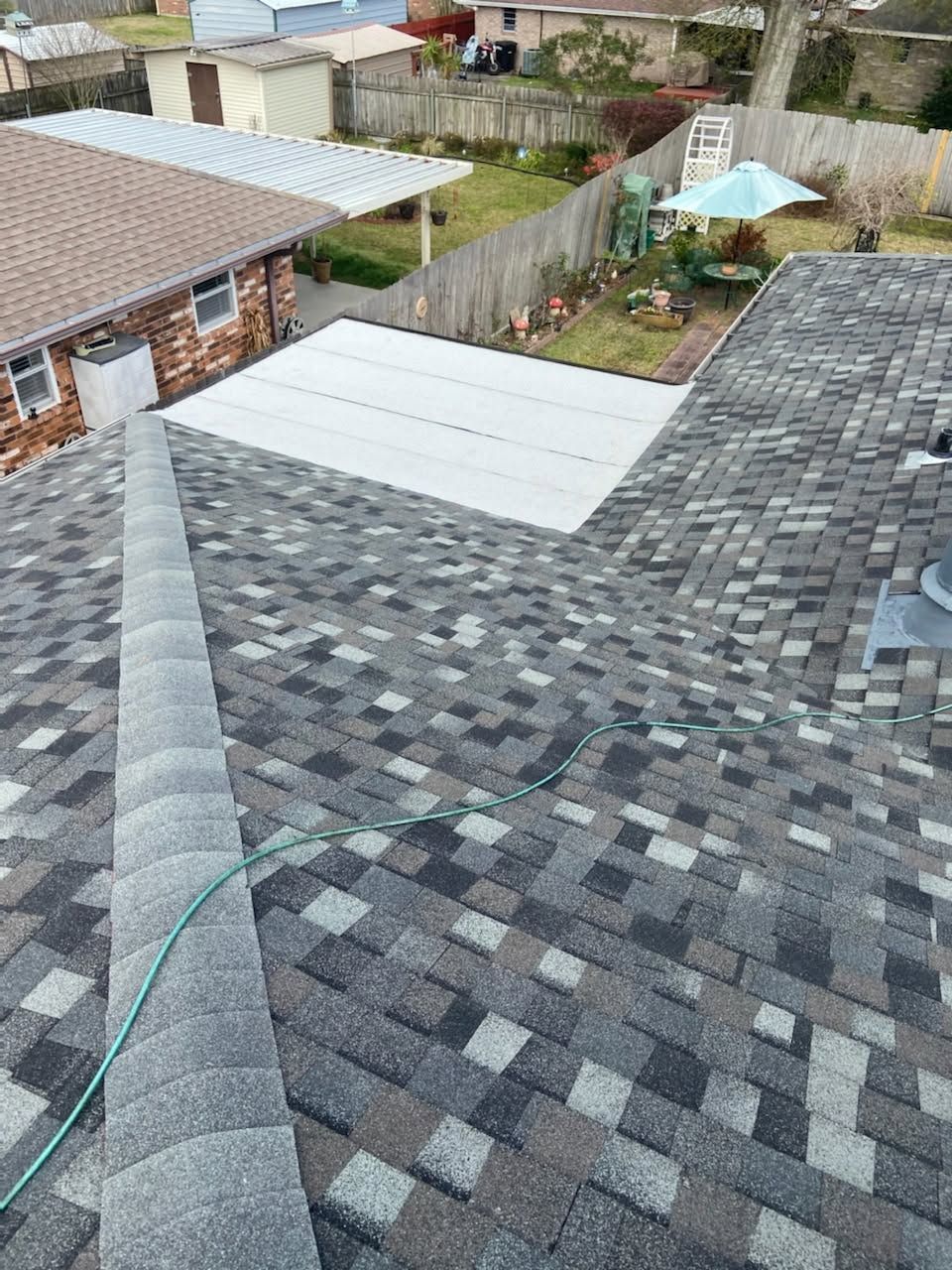 Rooftop with gray shingles and a white metal panel, overlooking a backyard and neighboring houses.