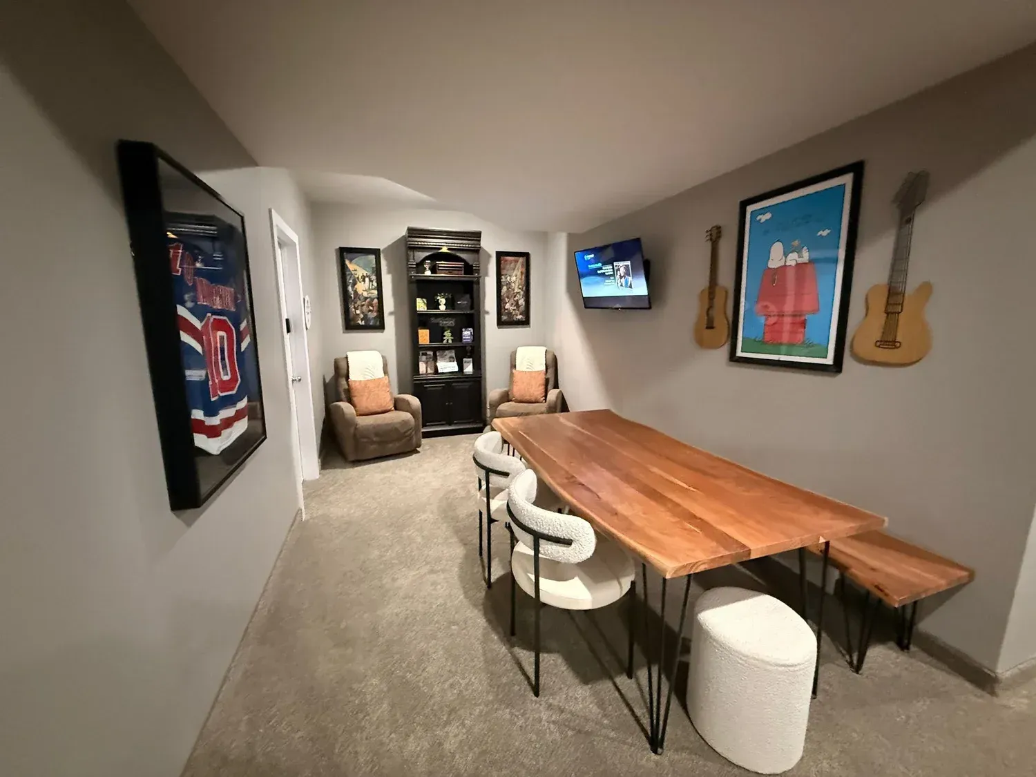 Narrow game room with long wooden table, chairs, wall art, TV, and a lounge chair at the far end.