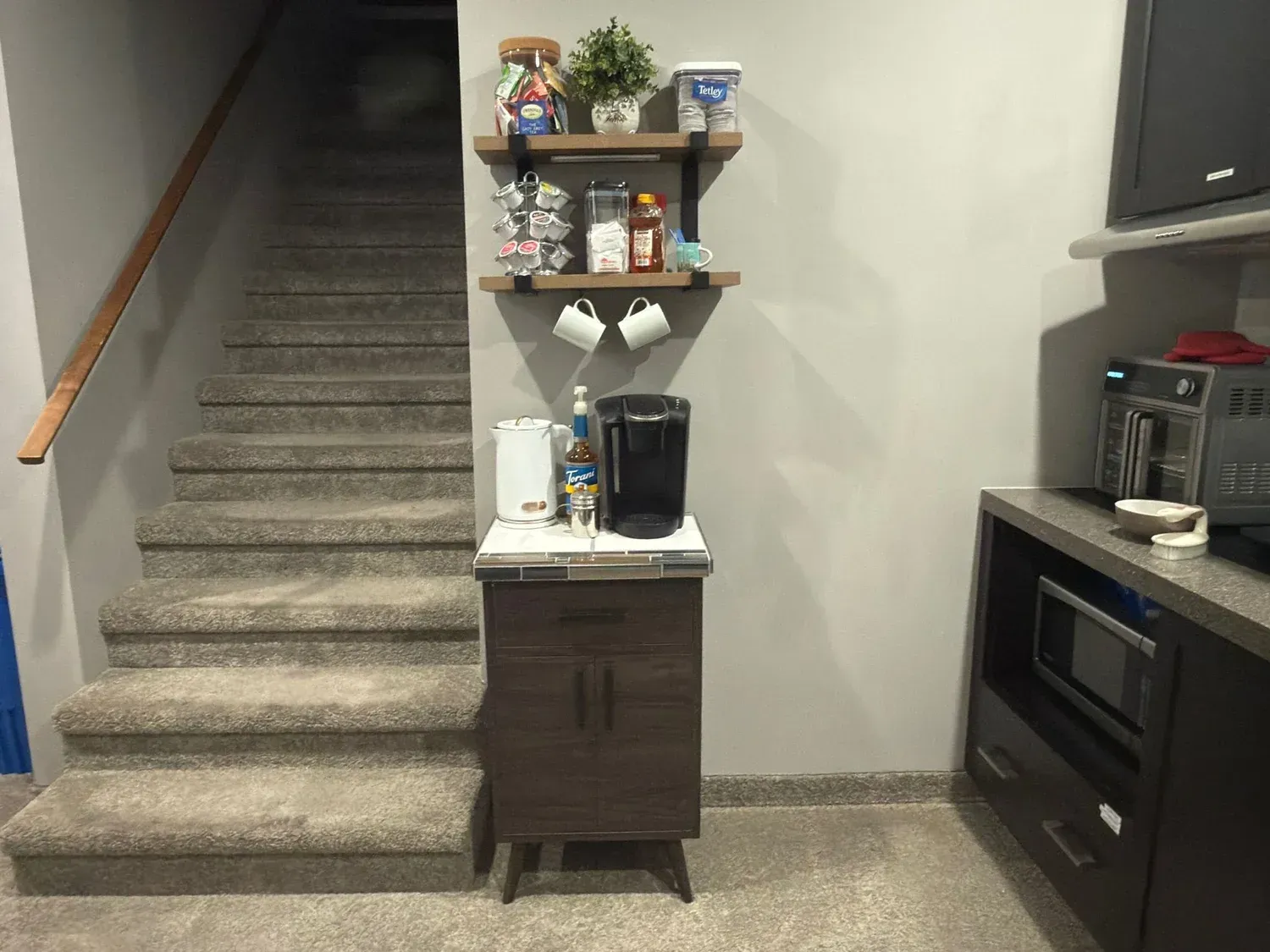 Carpeted basement stairway beside a small shelf and cabinet, with a black oven and TV on the right.