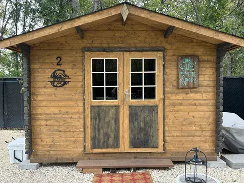 Small wooden shed with double doors and windows in a wooded yard.